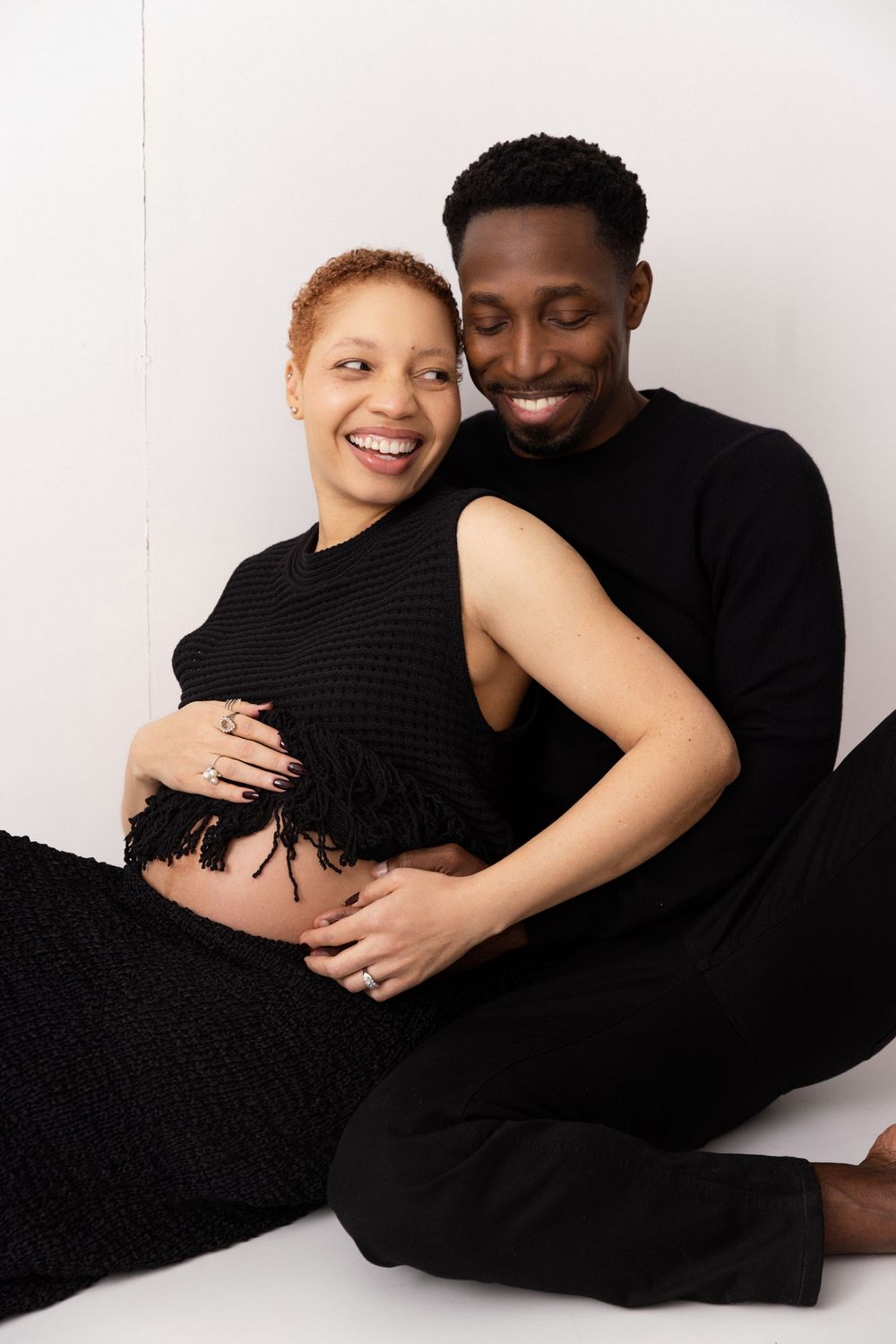Intimate maternity photo series of an expecting couple in black clothing against white background.
