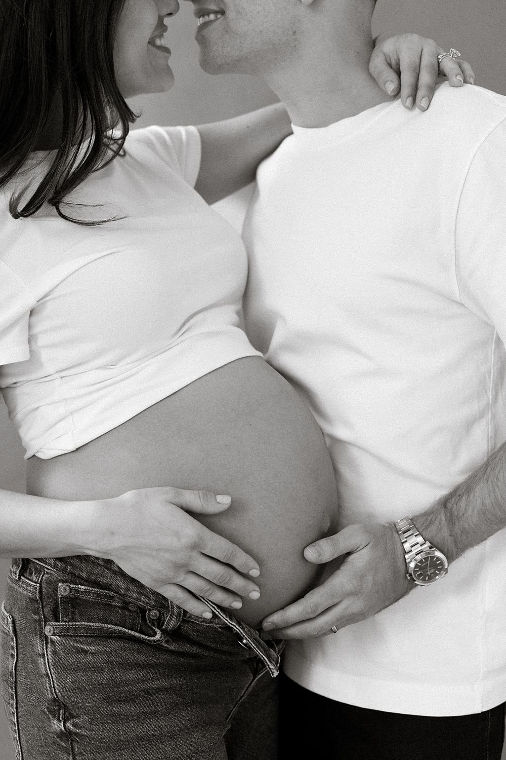Black and white pregnancy progression photos showing growing baby bump in white shirt and jeans over time.