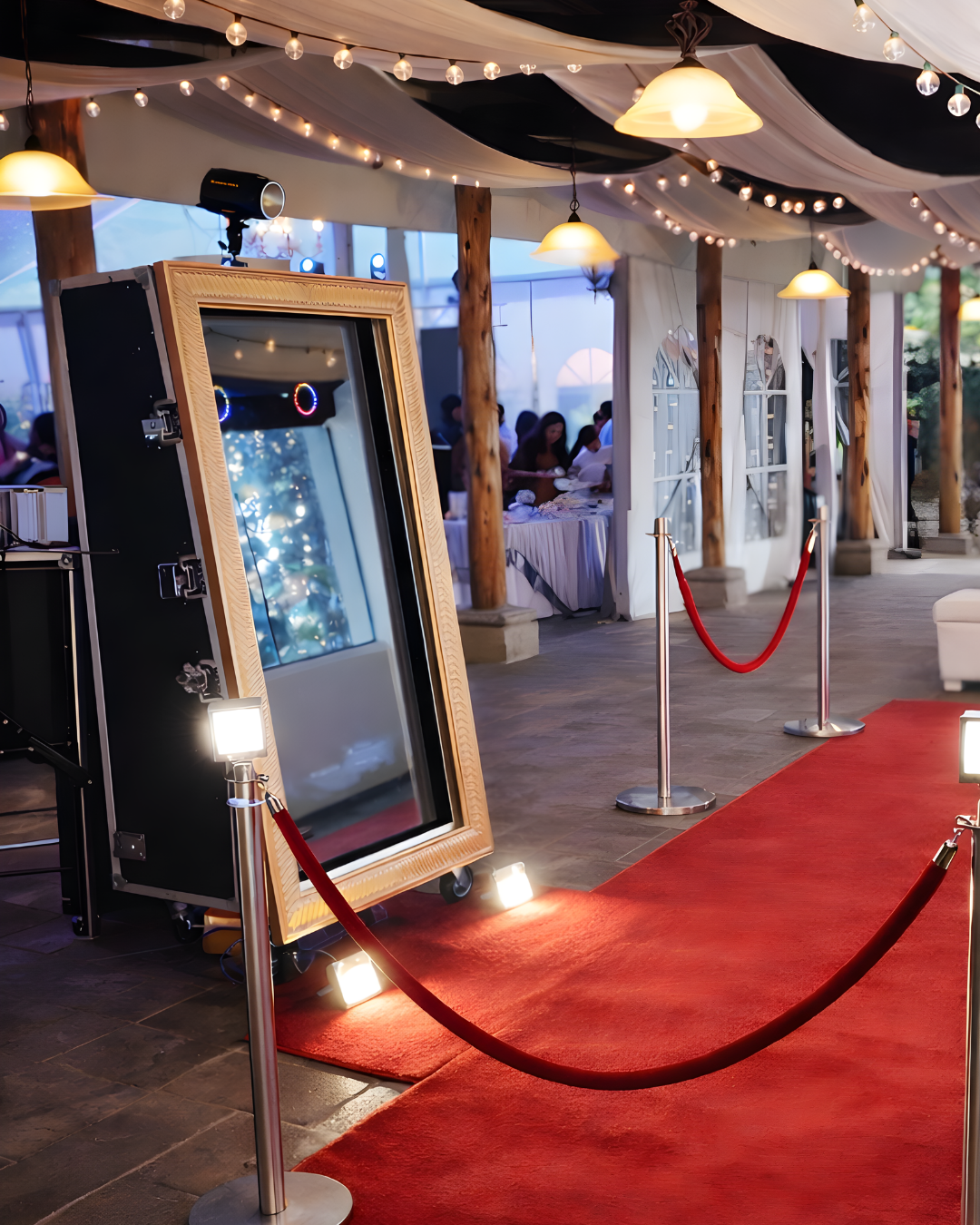 Red carpet walkway with stanchions and string lights creates an elegant event entrance with digital displays mounted along walls.