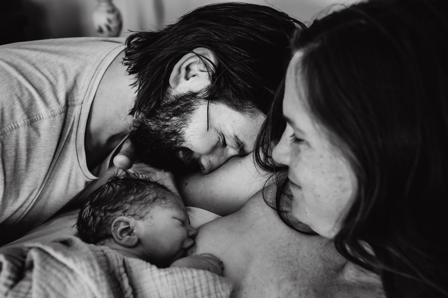 Father smiling with his wife and newborn baby moments after birth, capturing the raw emotion of a birth photography