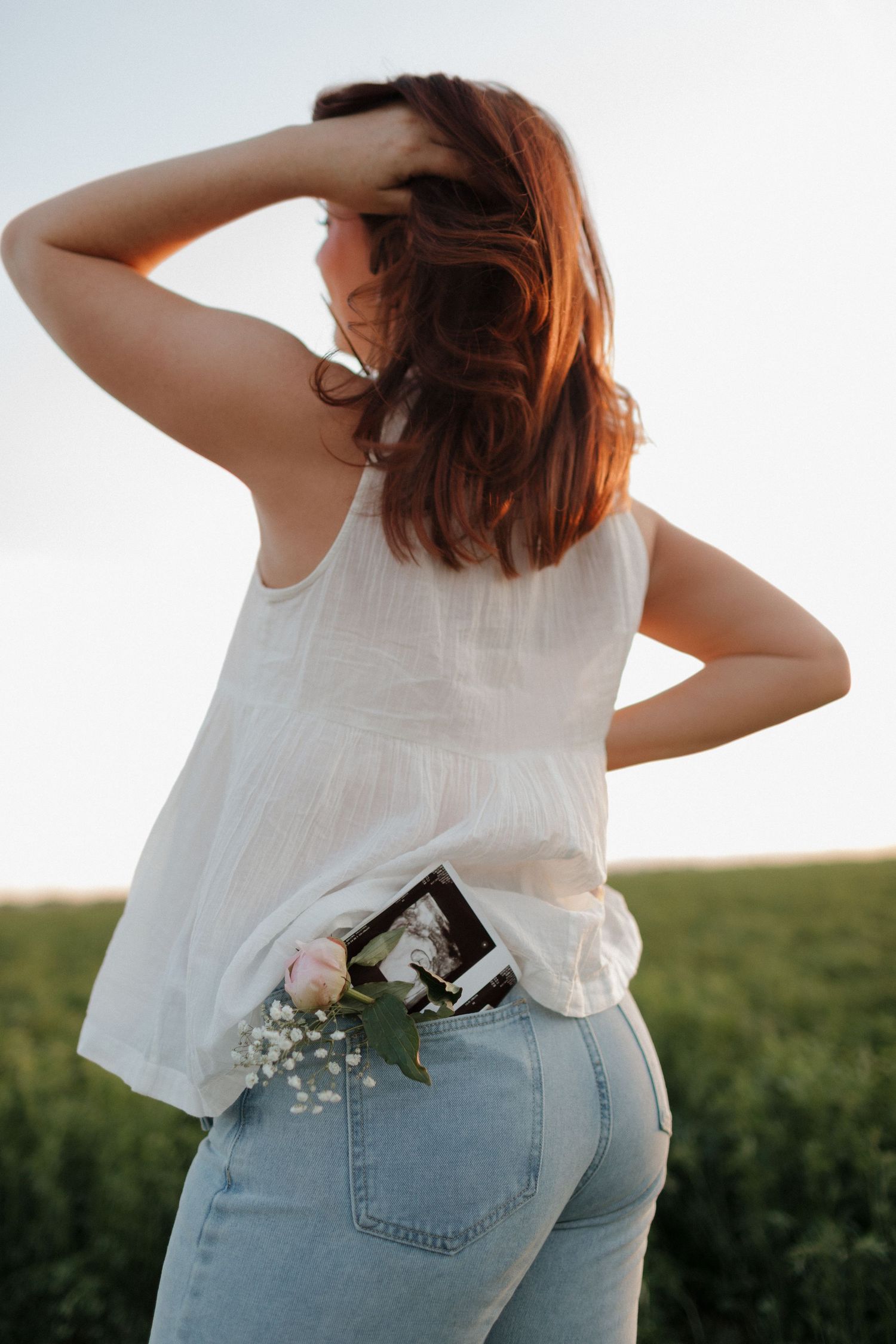 A close-up of hands cradling a pregnant belly while wearing casual denim and white clothing.