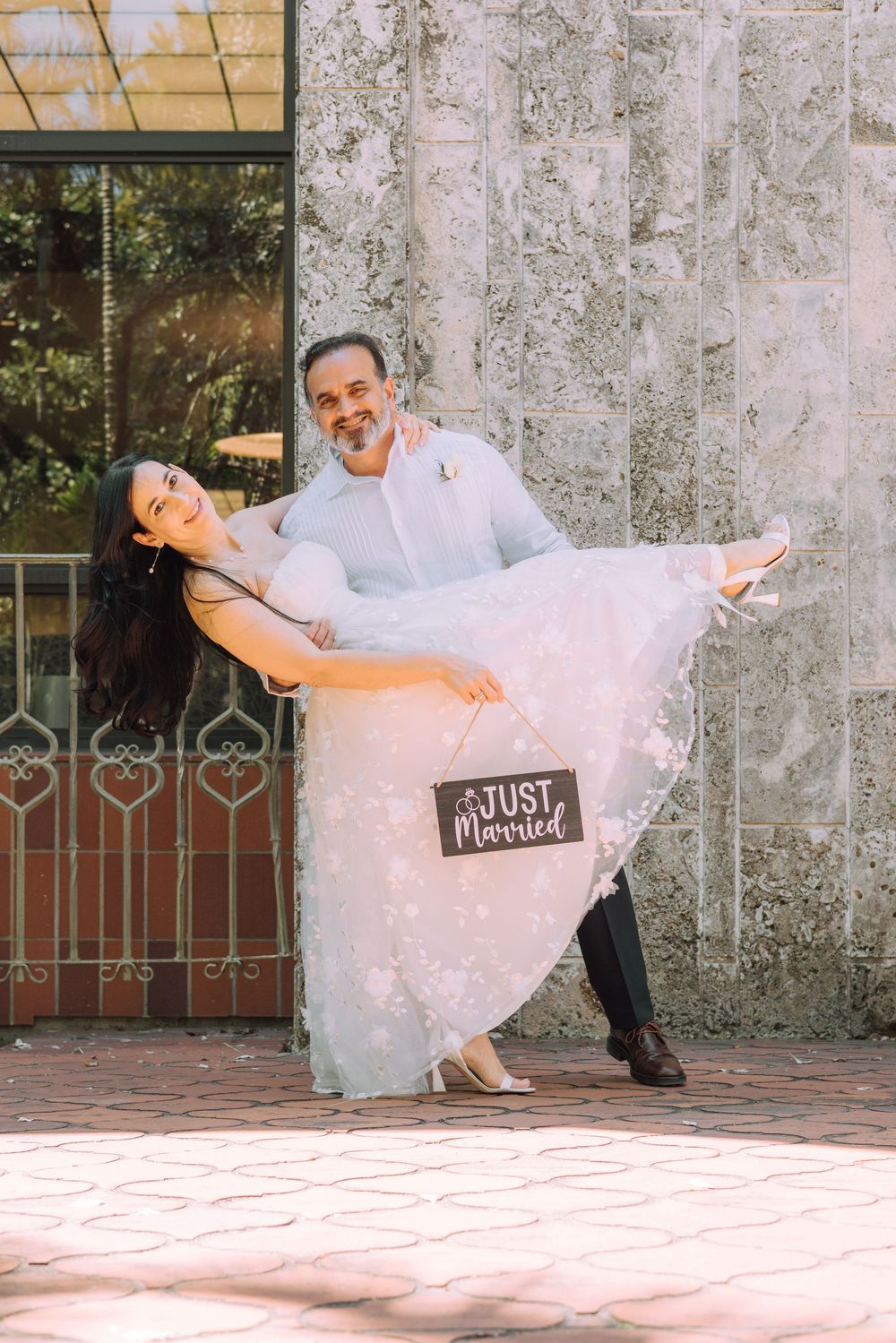 A couple in wedding attire dances romantically against a textured wall with decorative ironwork.