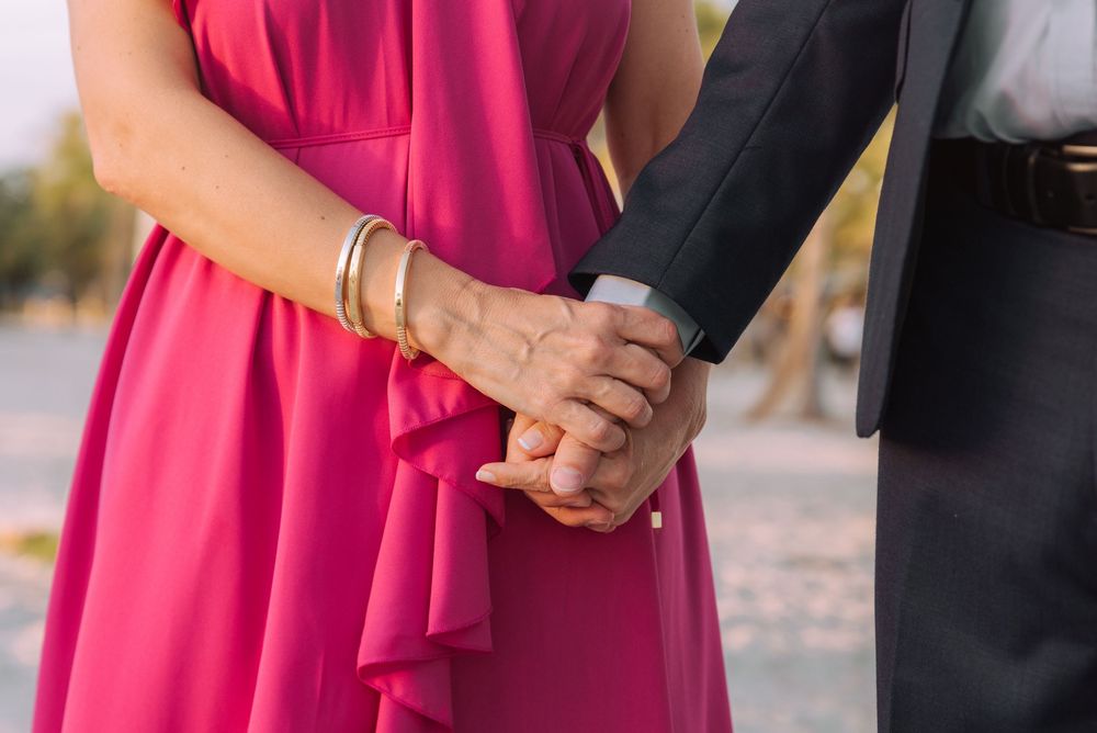 A couple holding hands, with the woman wearing a bright pink dress and the man in a black suit.