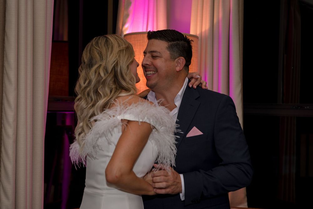 A couple shares a romantic moment on the dance floor with soft pink lighting at their wedding reception.