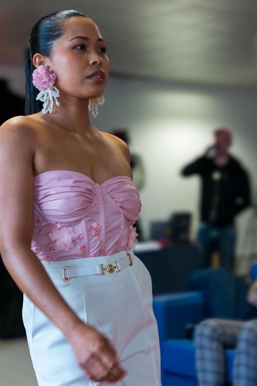 A person wearing a pink and white formal dress with elegant styling and accessories stands in an indoor setting.