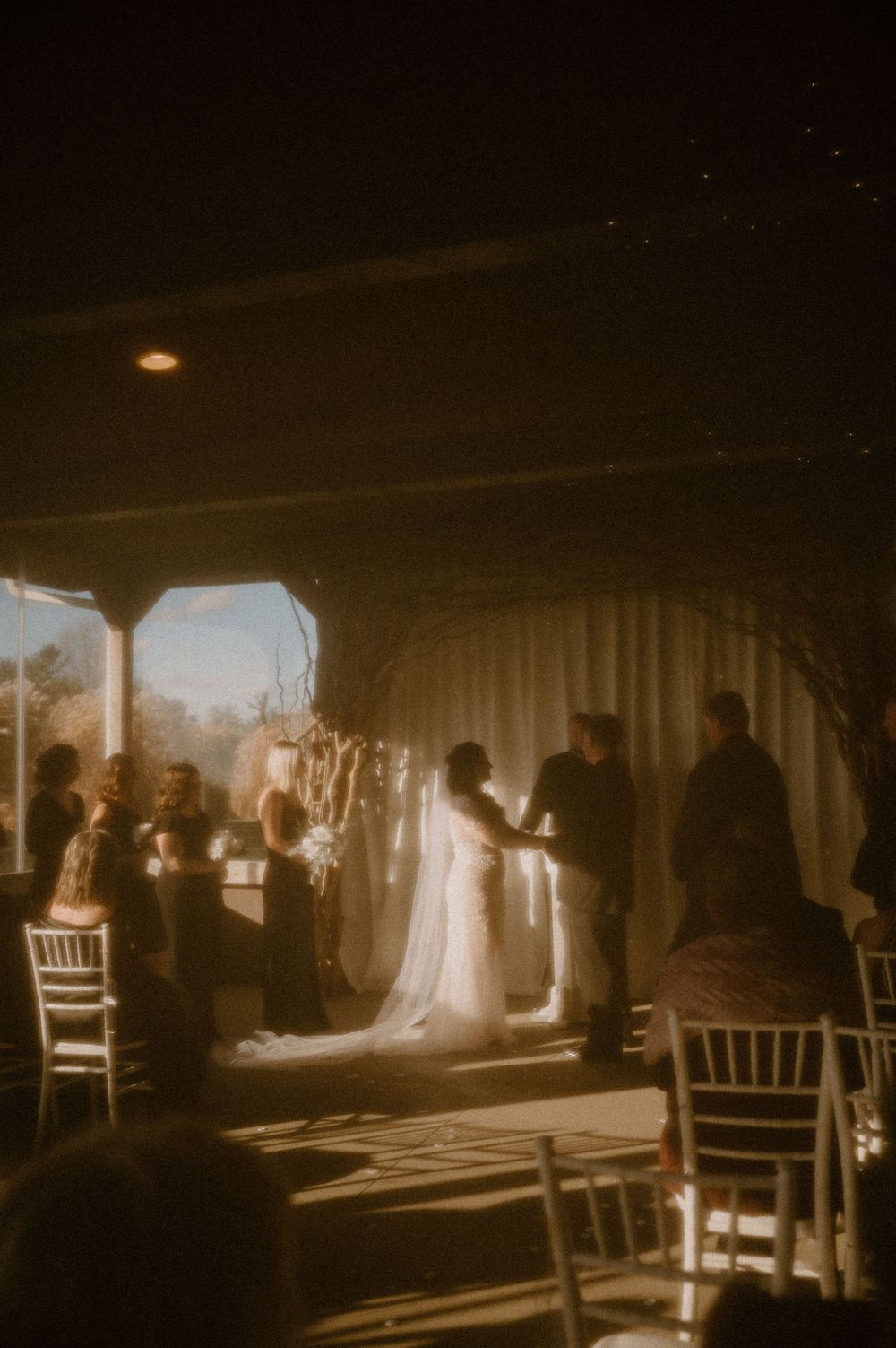 A wedding ceremony silhouette at sunset with light streaming through a covered venue with white chairs.