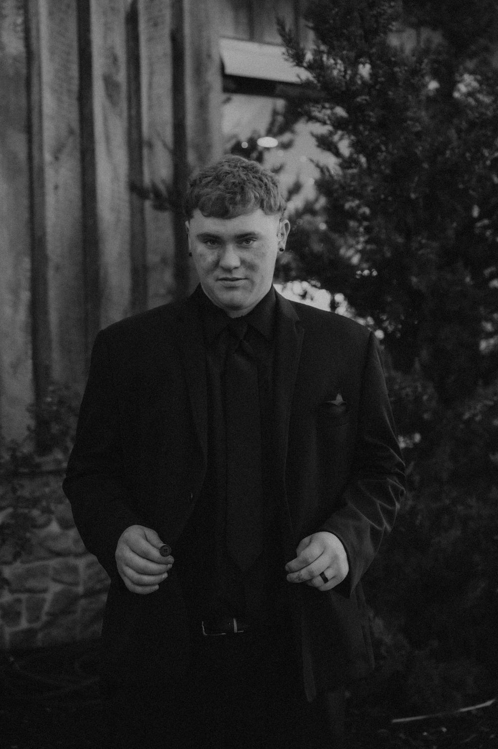Black and white photograph of a person wearing a dark coat standing in a wooded area.