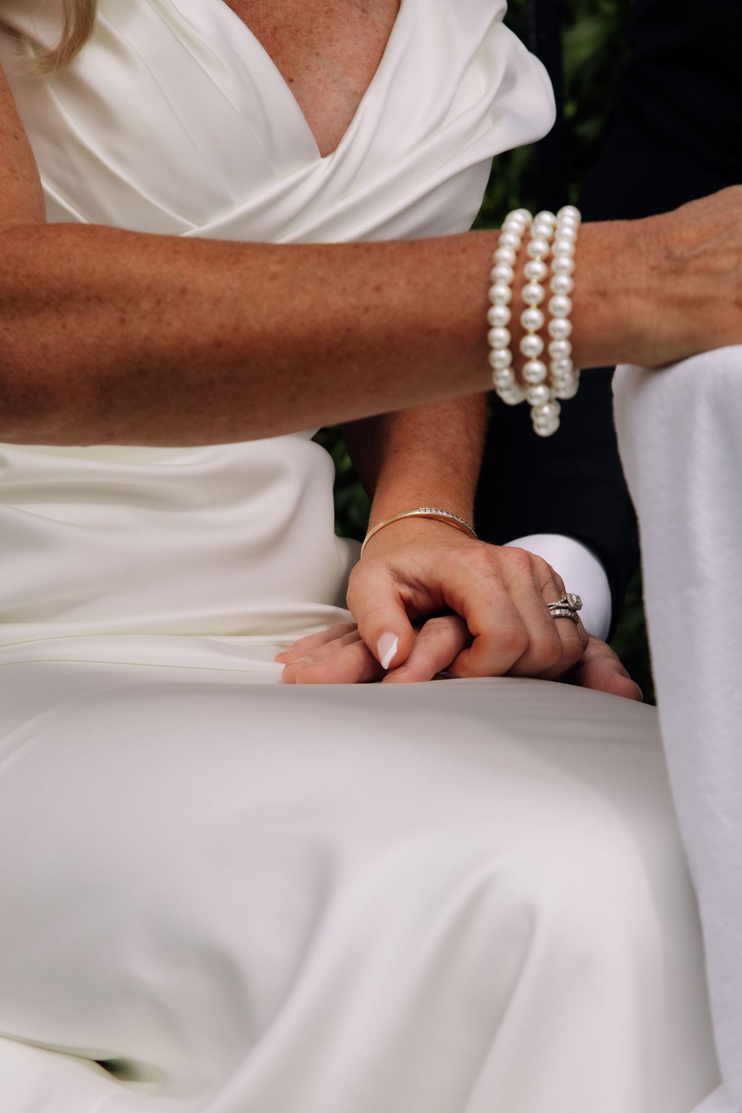 Close-up details of a white wedding dress with pearl bracelet accessories and elegant hand positioning.