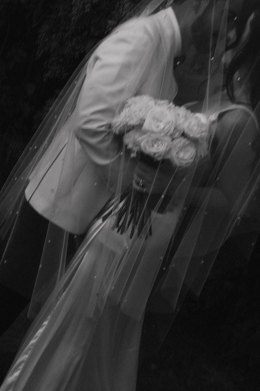 A bride and groom hold hands during a wedding ceremony in a dramatic black and white photograph.
