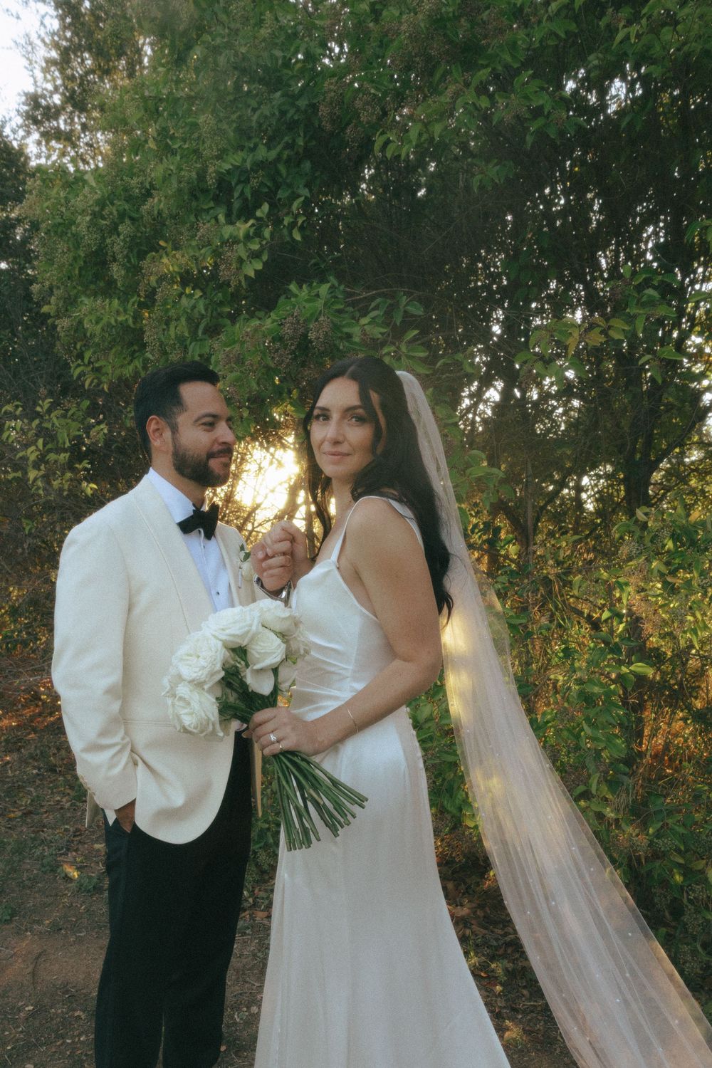 A bride and groom share romantic moments in an outdoor garden setting with lush greenery and golden sunlight.