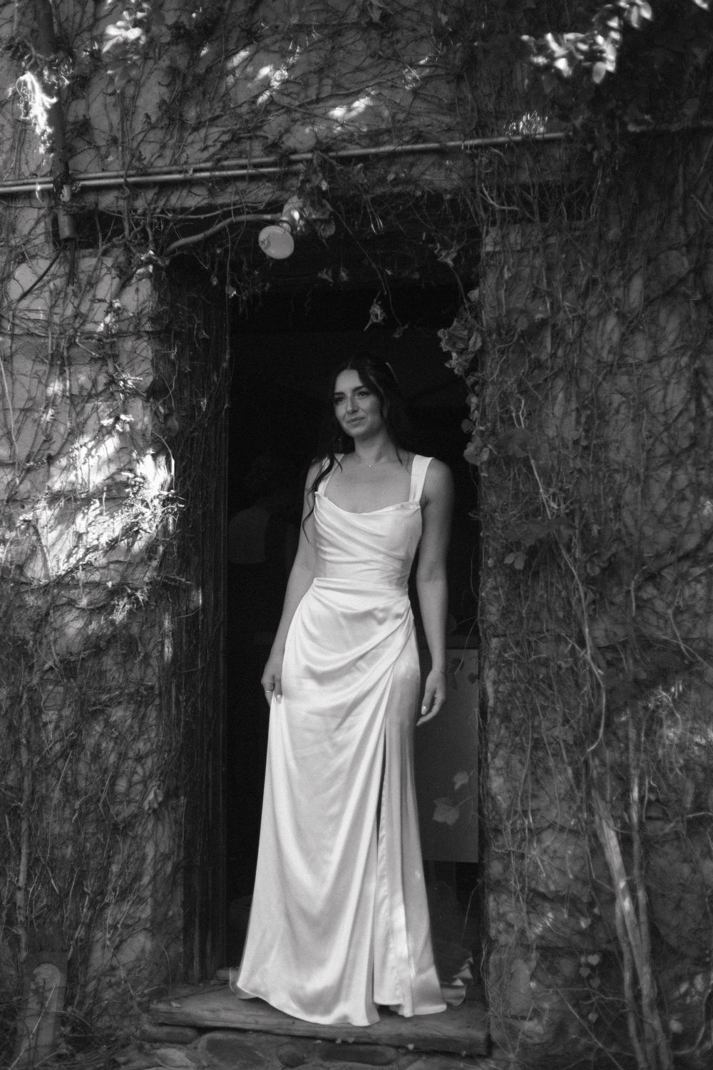 A series of black and white photographs showing someone in a white dress standing against a stone wall with vines.