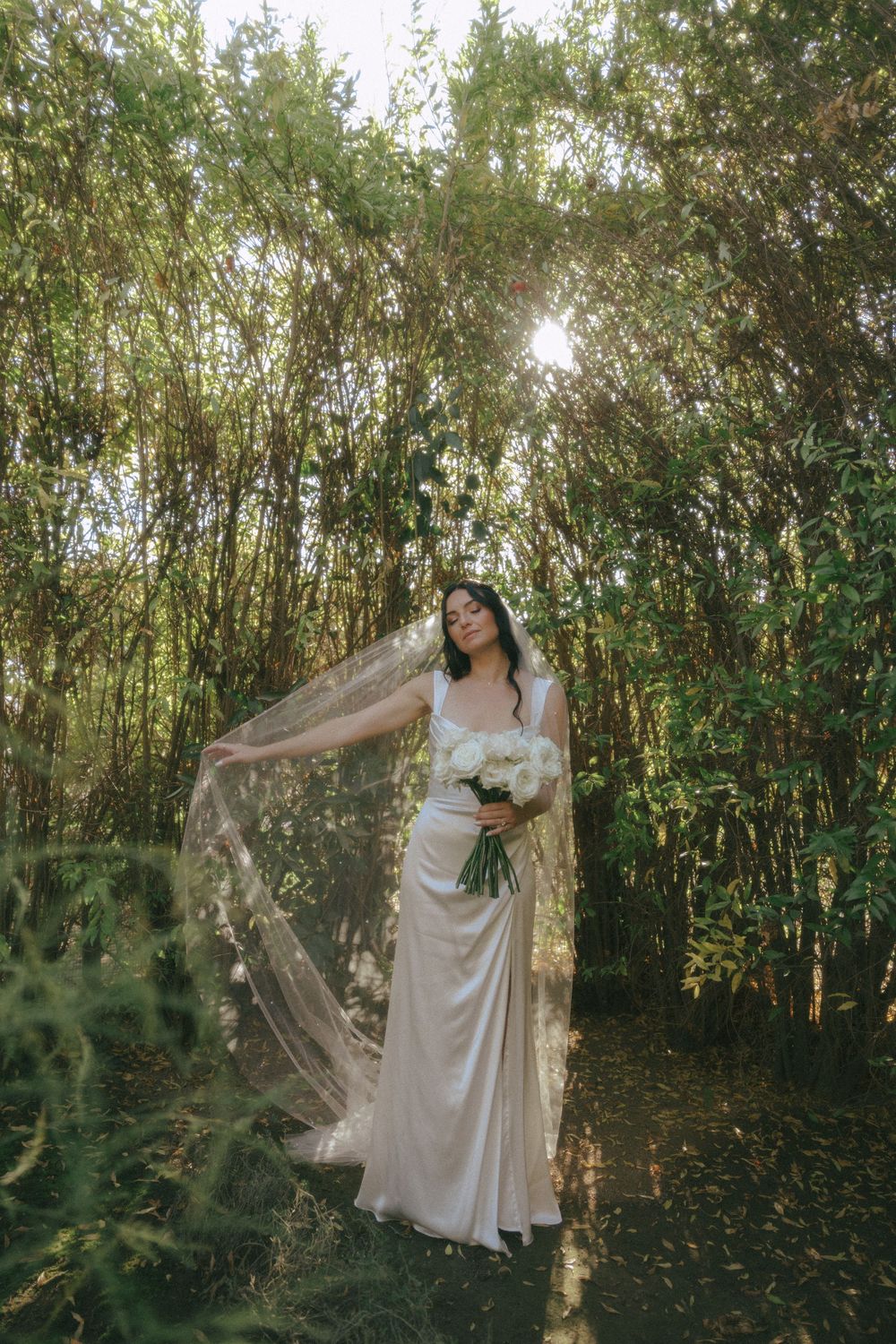 A dreamy bridal portrait in a bamboo forest with flowing white dress and veil catching sunlight through the trees.
