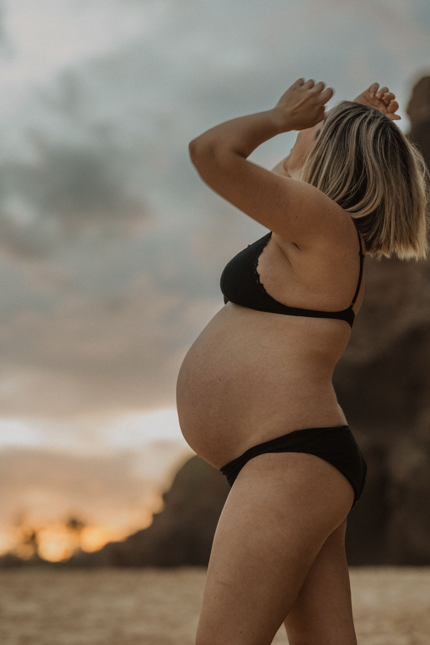 Silhouette of an expectant mother in black swimwear against a sunset sky.