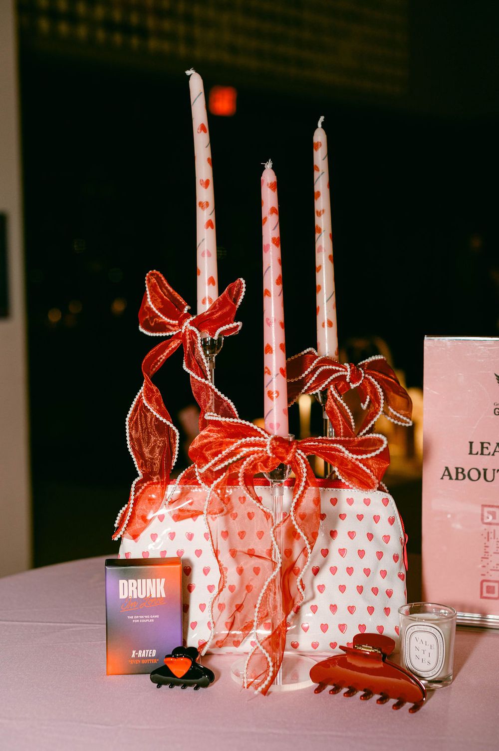 Valentine's Day themed gift bags and candles arranged in a row with red bows and heart patterns.