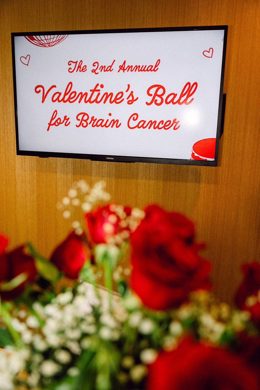 Red and white Valentine's Ball signage displayed above elegant floral arrangements with roses and baby's breath.