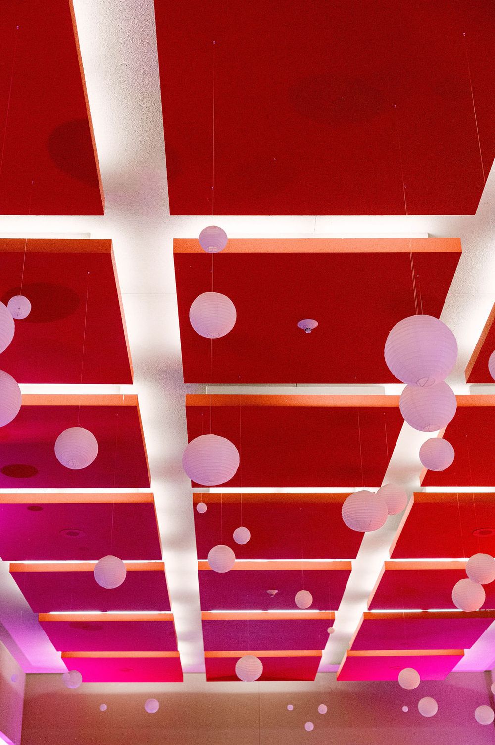 Abstract architectural interior with red ceiling beams and floating white spheres creating a modern, dynamic space.