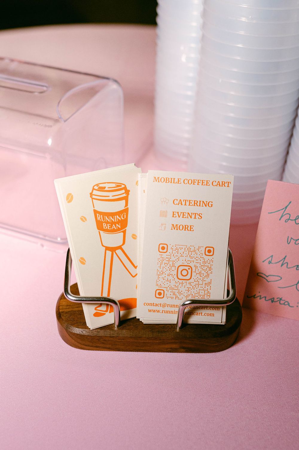 Business cards for a mobile coffee cart and catering service displayed on a pink surface with white cups in the background.