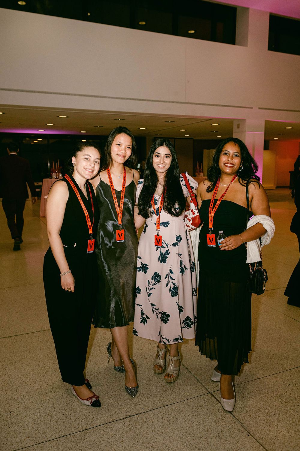 A group of friends pose together in formal attire at what appears to be an indoor venue or event space.