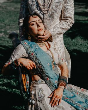 Person in elegant blue and white embroidered dress poses against tree trunk in dramatic sunlit setting.