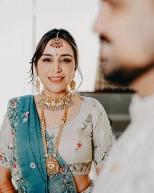 Bride wearing traditional Indian wedding attire in teal and cream with ornate gold jewelry and bindi in candid shots.