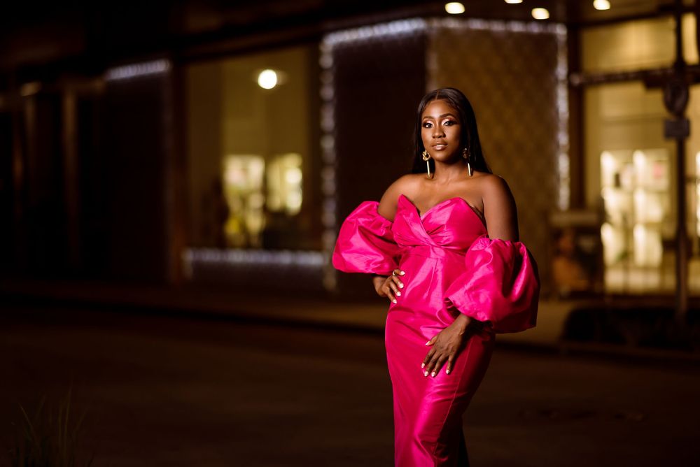 A figure in a vibrant hot pink evening gown with dramatic puff sleeves poses on a city street at night.