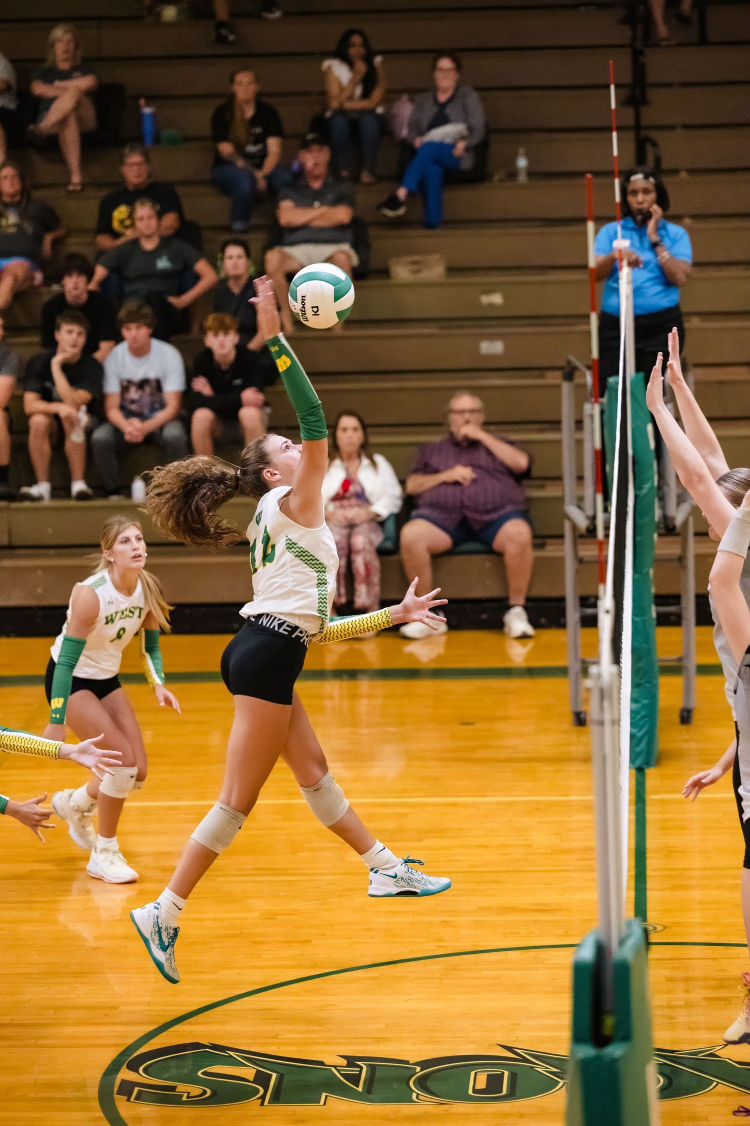 Volleyball players in action during a match with spectators watching from bleachers.