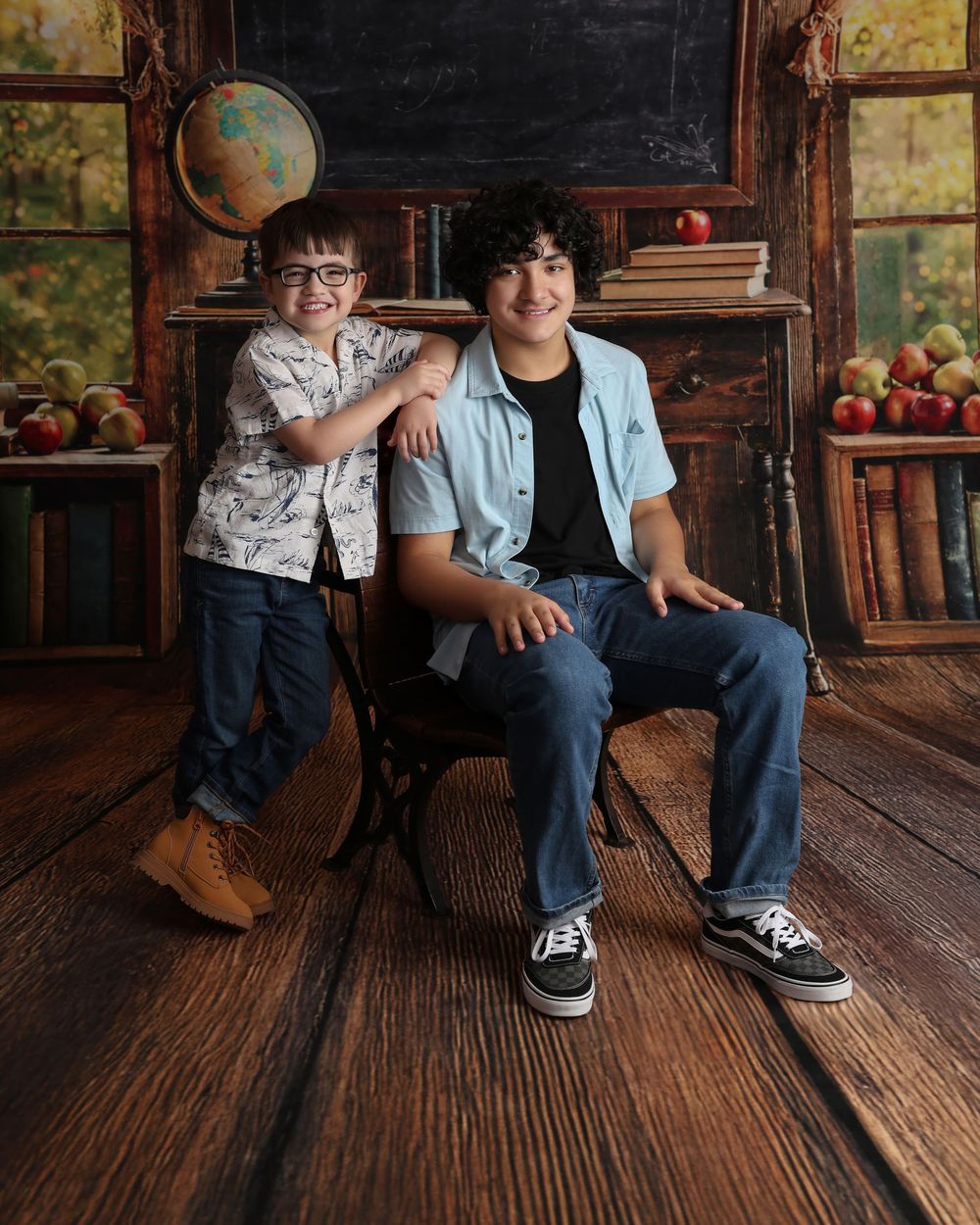 Two smiling boys pose in a school-themed portrait with books, apples, and a globe on a wooden floor in Covington, GA