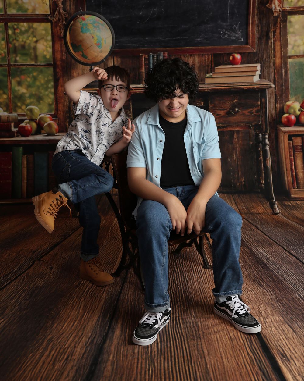 Two playful boys pose in a rustic classroom setting with books, apples, and a globe in the background in Covington, GA