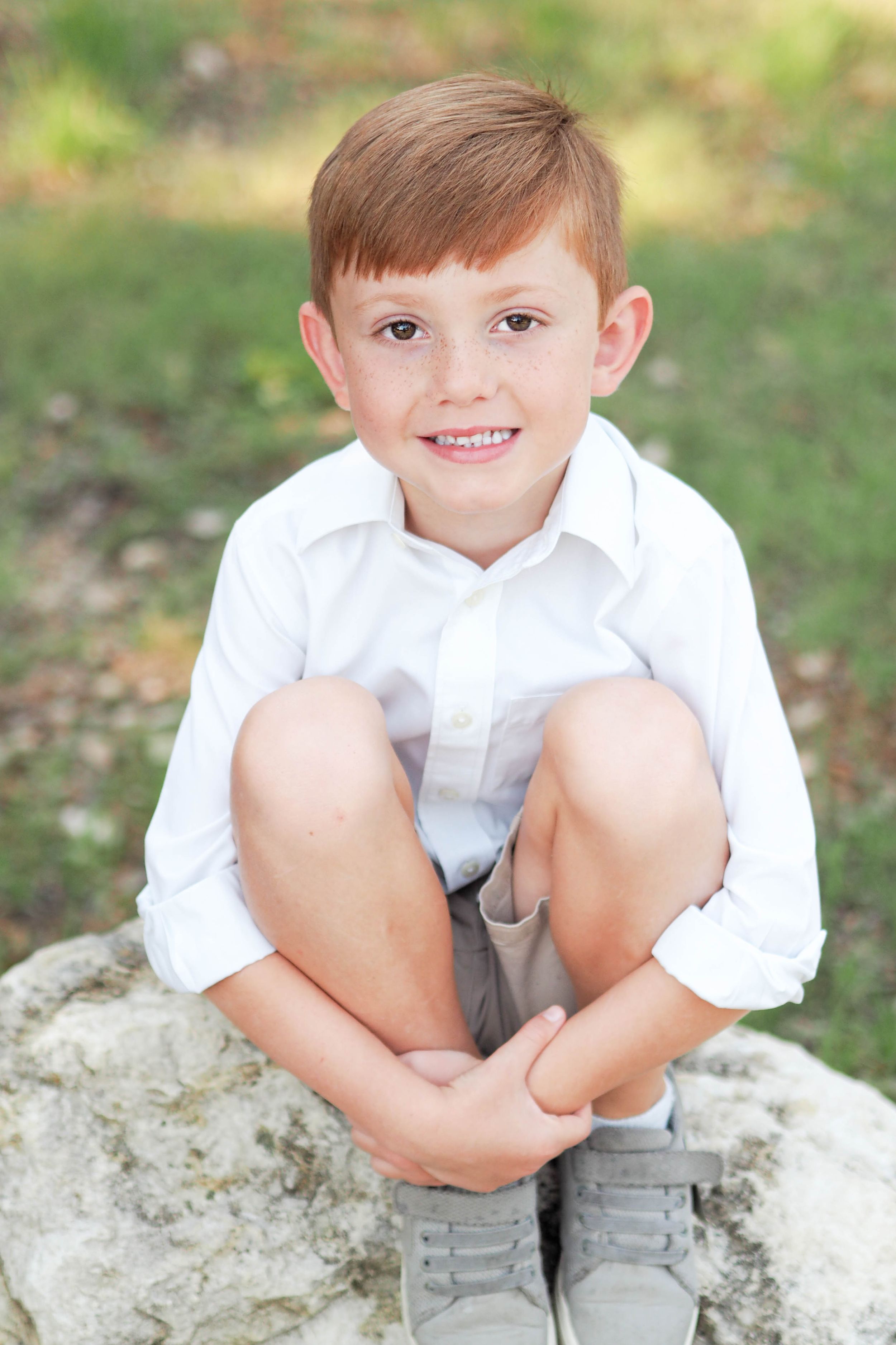 Spring photo of young boy sitting on rock, smiling.
