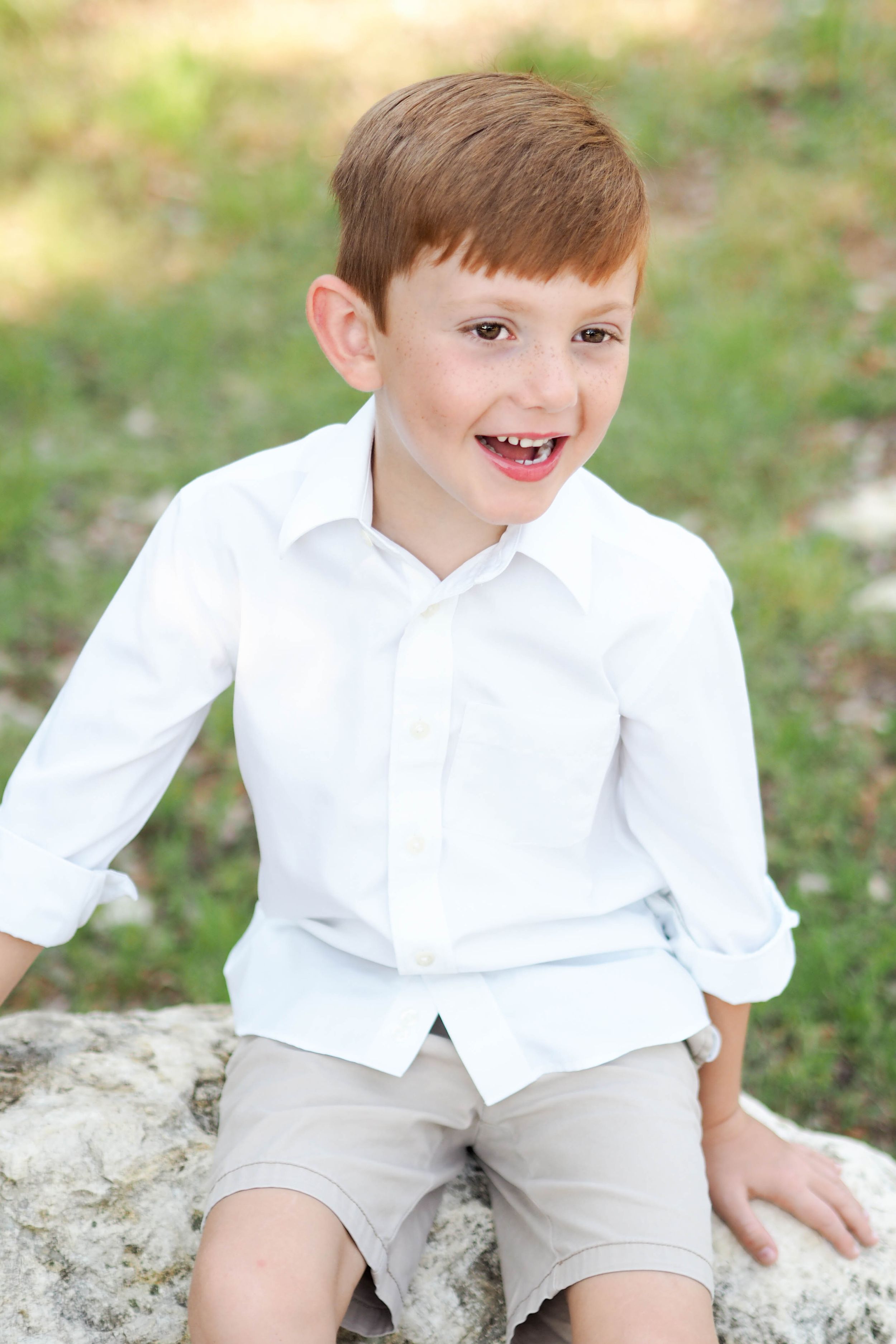Spring photo of young boy sitting on rock, laughing.