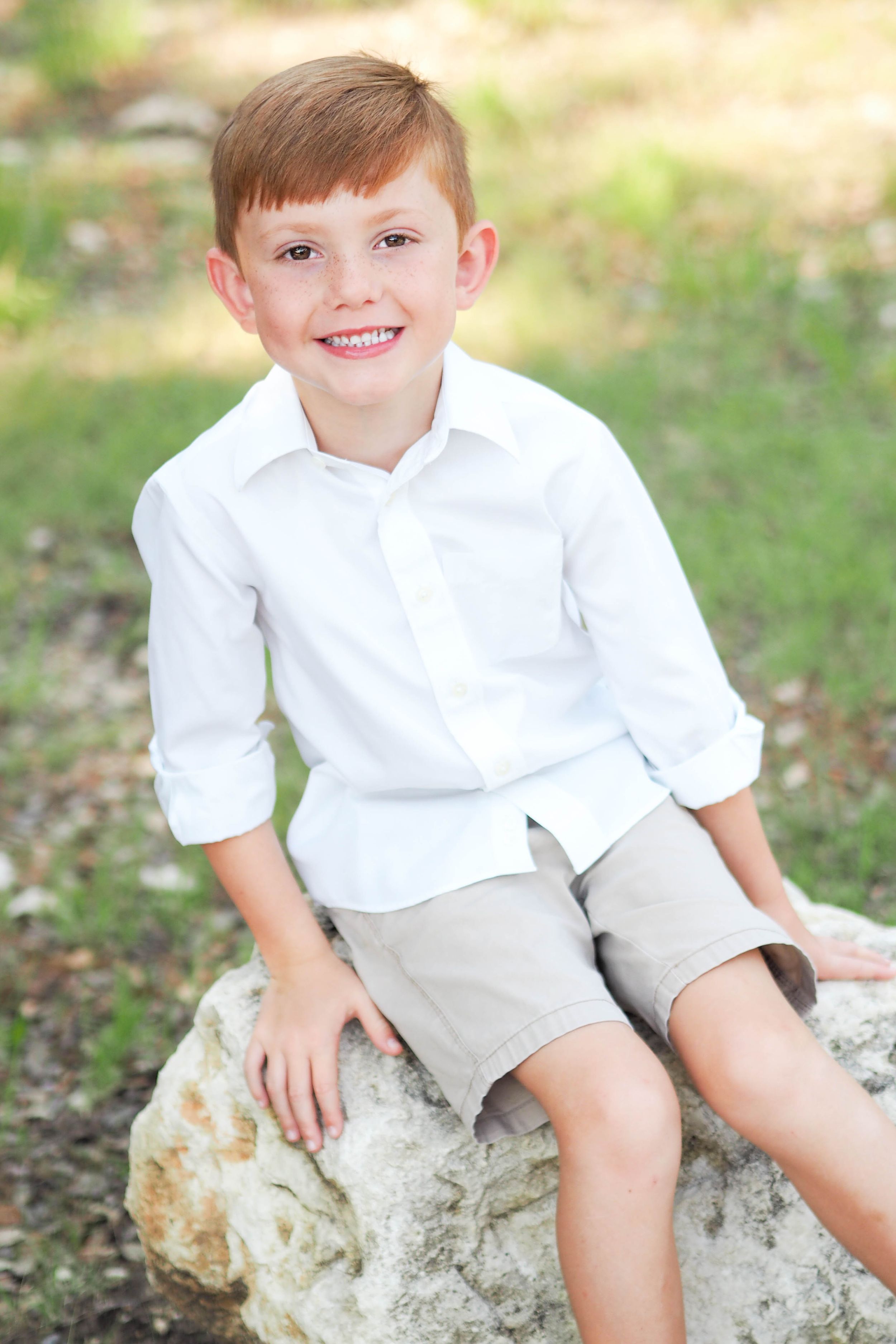 Spring photo of young boy sitting on rock, smiling.