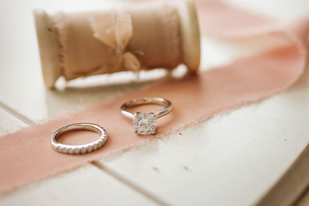 Elegant engagement ring and wedding band set displayed on soft pink fabric with delicate lighting.