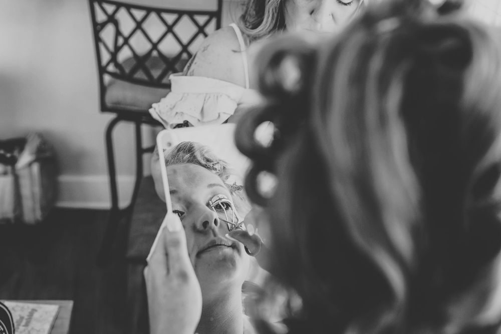 The bride curling her eye lashes in a mirror in black and white
