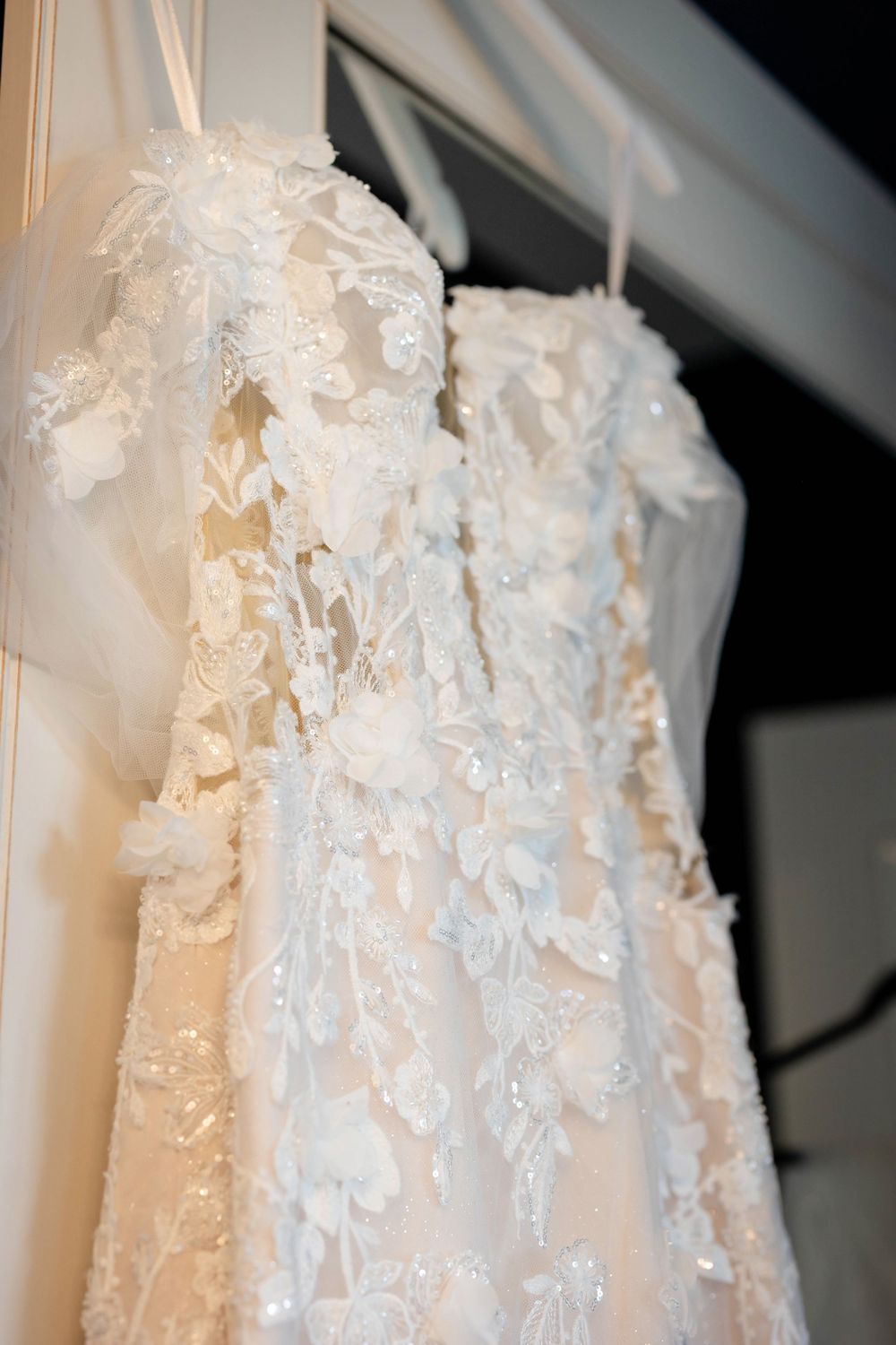 Close-up view of white lace wedding dresses hanging on display, showing intricate floral embroidery details.