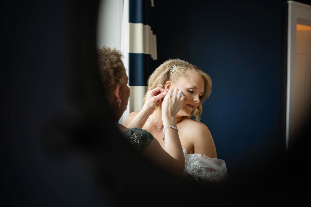 A reflection of a bride in a mirror putting on her earring in natural light