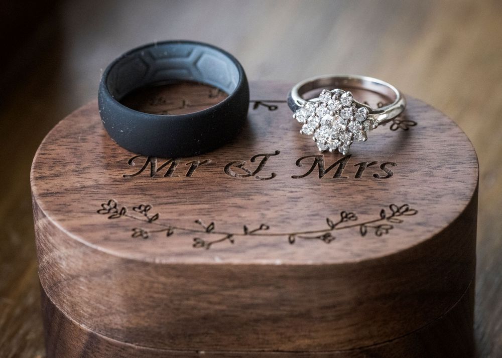 Wedding rings displayed on engraved wooden Mr. and Mrs. ring box, featuring a diamond cluster ring and silicone band.