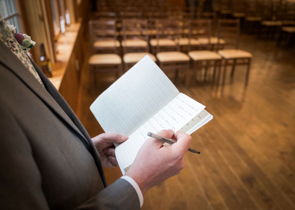Officiant reviewing handwritten notes in notebook inside rustic wooden ceremony venue before wedding.