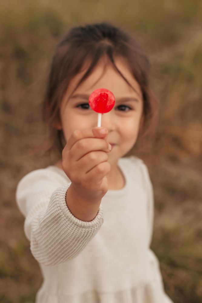 A person wearing a white sweater holds up a red flower against a blurred brown background |Westminster Colorado Family Photographer