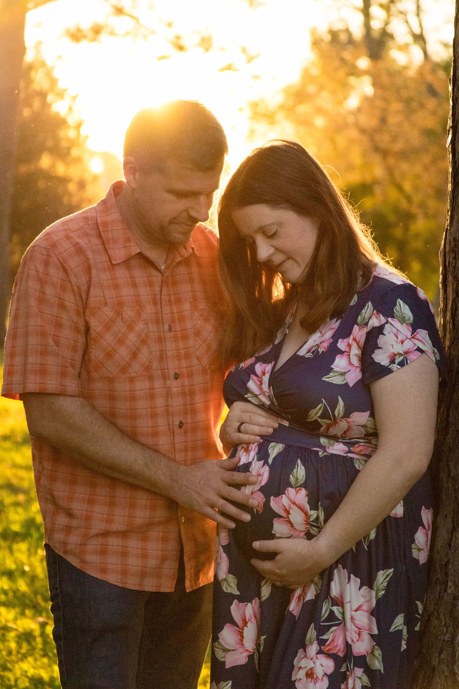 Couple shares intimate moment at sunset in a field with warm golden light glowing through trees.