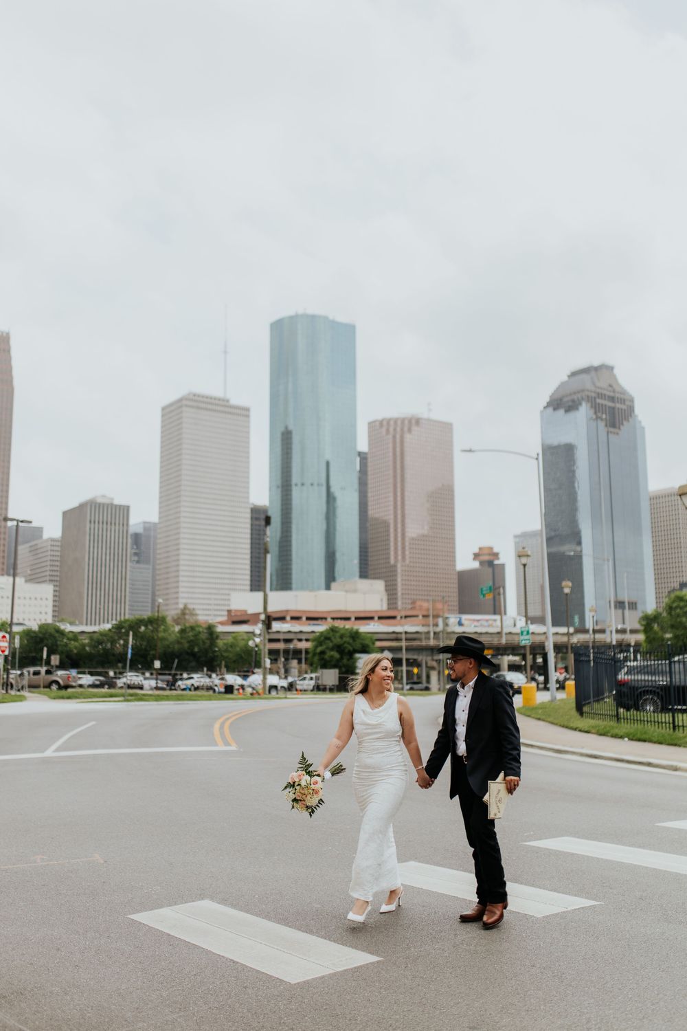 A couple in wedding attire poses for creative photos with the Houston skyline in the background.