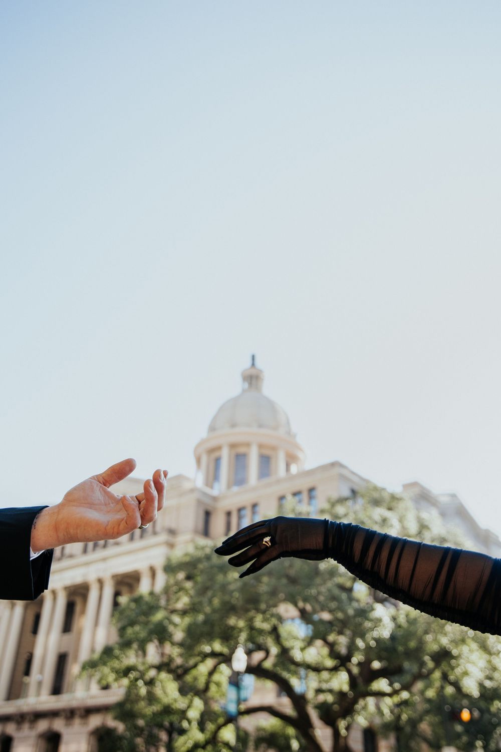 Hand pointing towards a historic domed building with ornate architecture against a blue sky.
