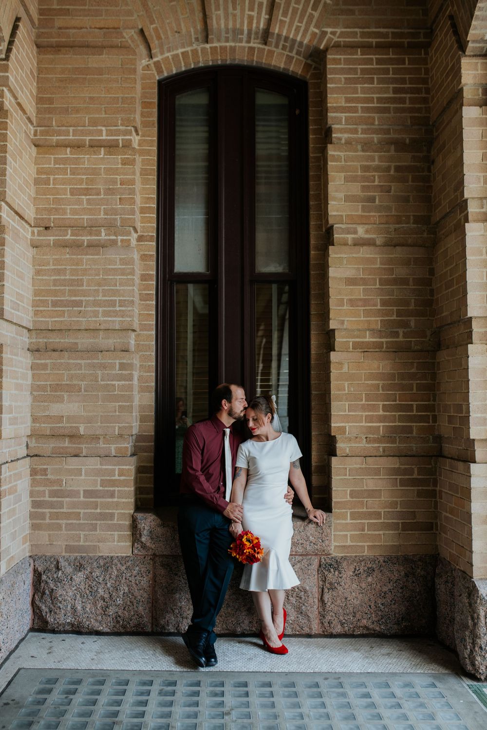 Three romantic photos of a couple sitting in an arched brick colonnade wearing formal attire and red shoes.