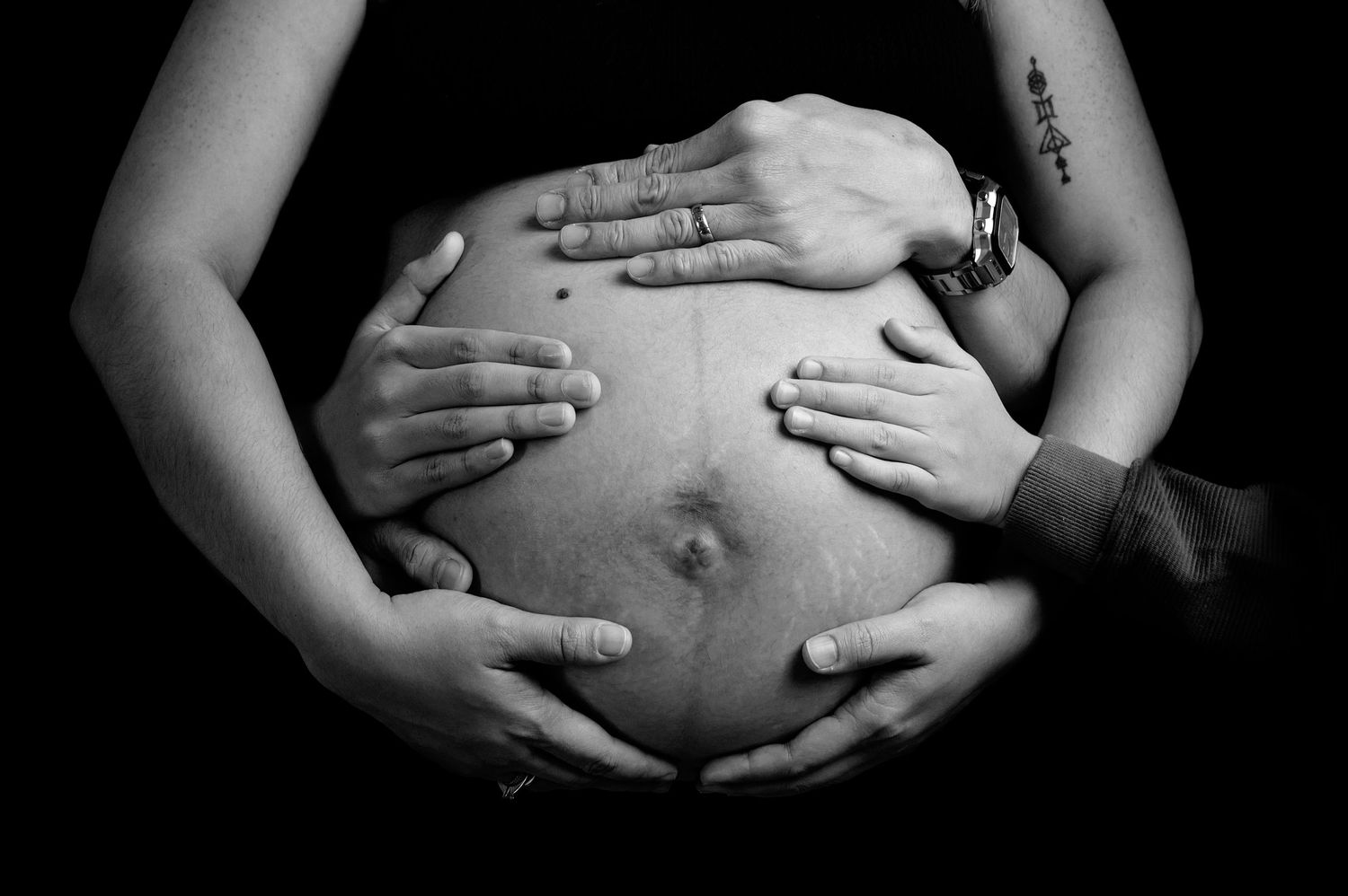 A series of black and white photos showing hands gently cradling a pregnant belly in different positions.