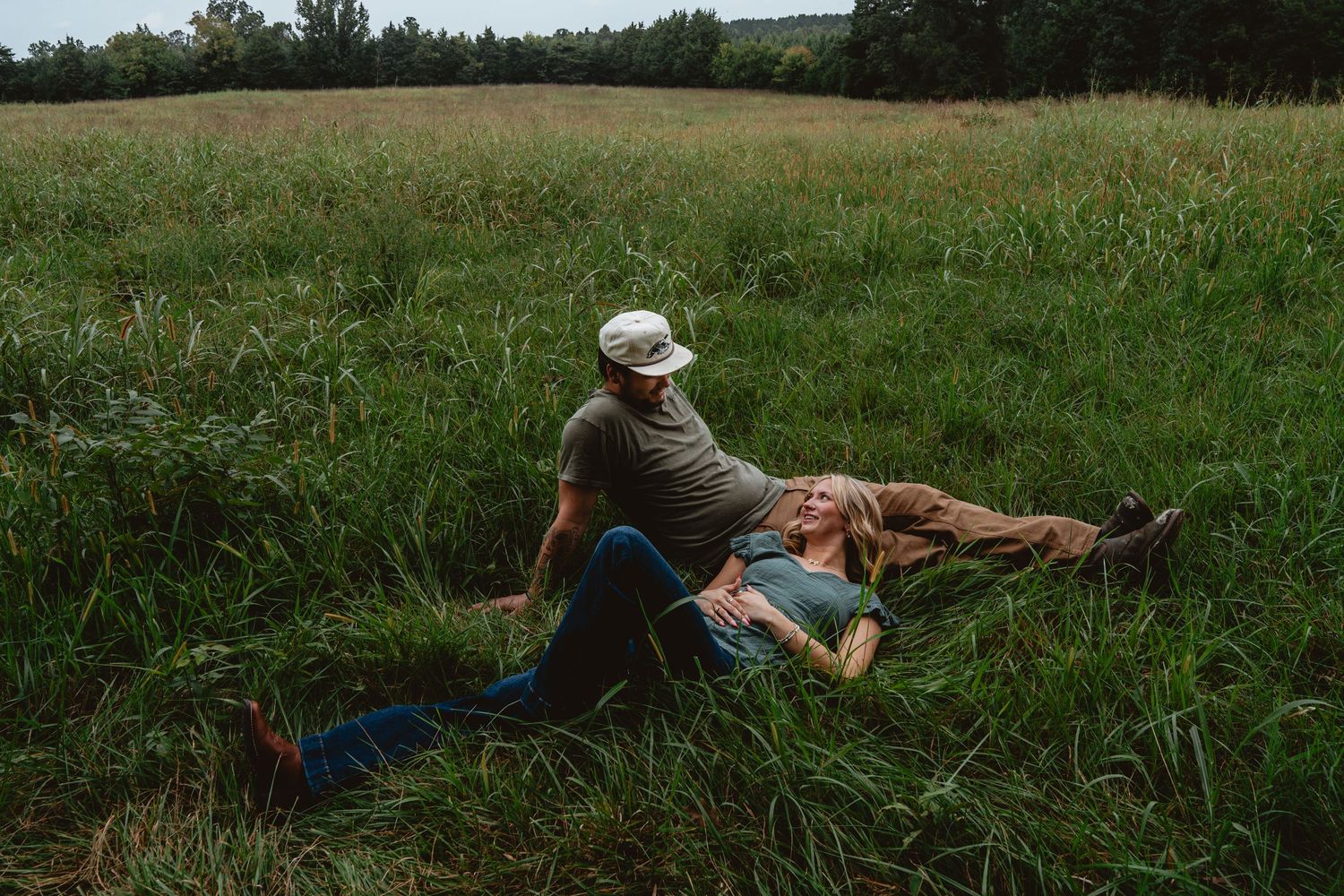 Couple embracing in a scenic field of tall grass with cloudy skies overhead.