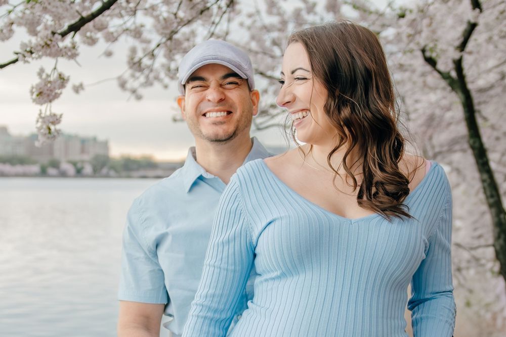 Couples walking under pink cherry blossoms along the Tidal Basin waterfront during peak bloom.