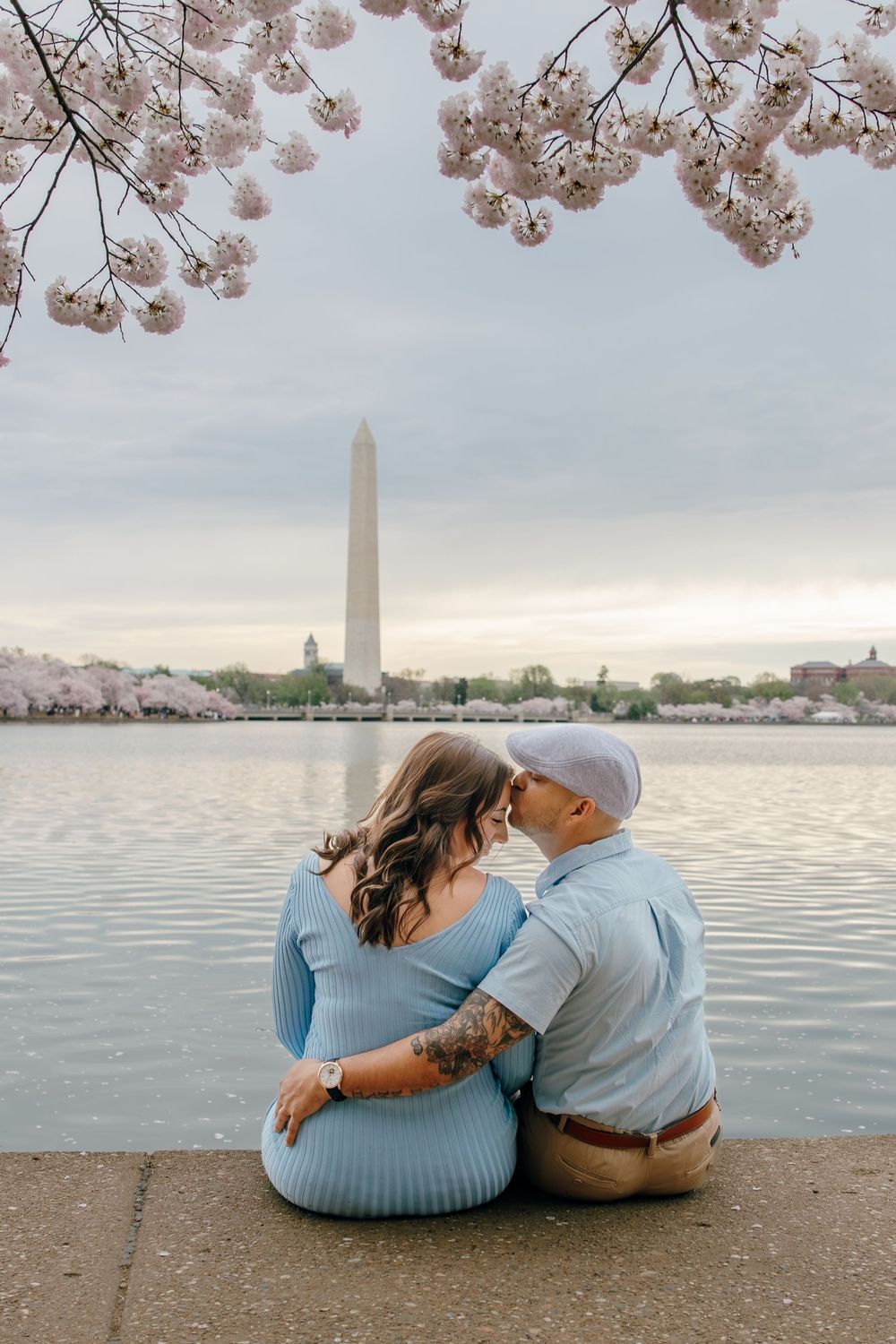 Couples walking under pink cherry blossoms along the Tidal Basin waterfront during peak bloom.