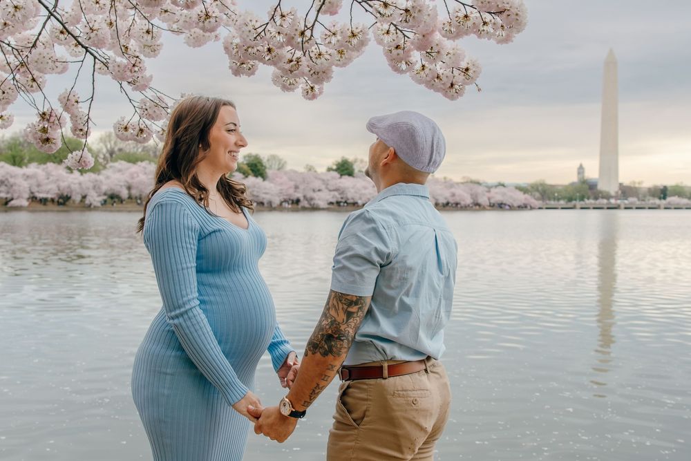 Couples walking under pink cherry blossoms along the Tidal Basin waterfront during peak bloom.