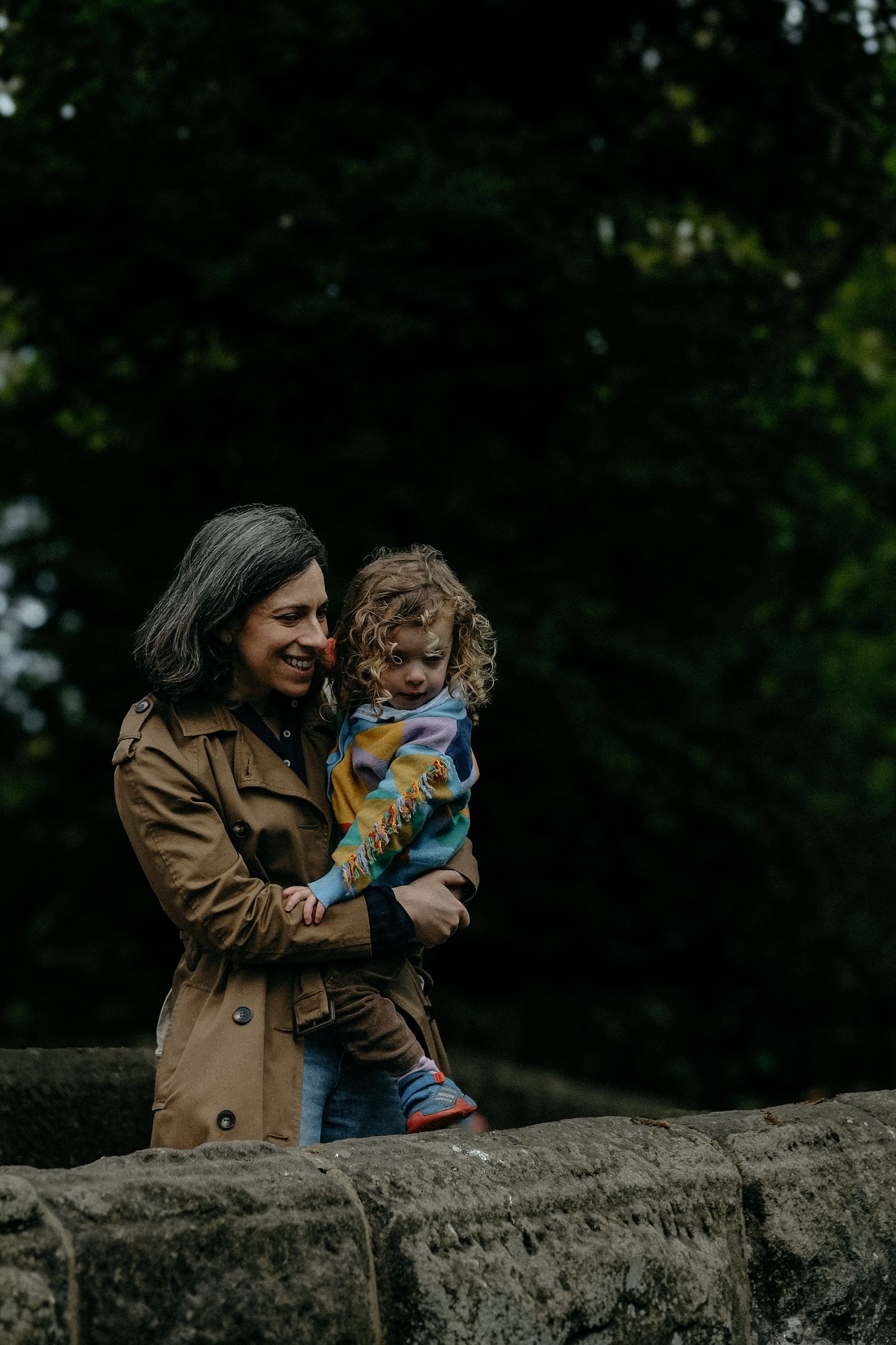 A mother holding her young child close among stone steps and greenery, sharing a tender moment during an outdoor family portrait session.