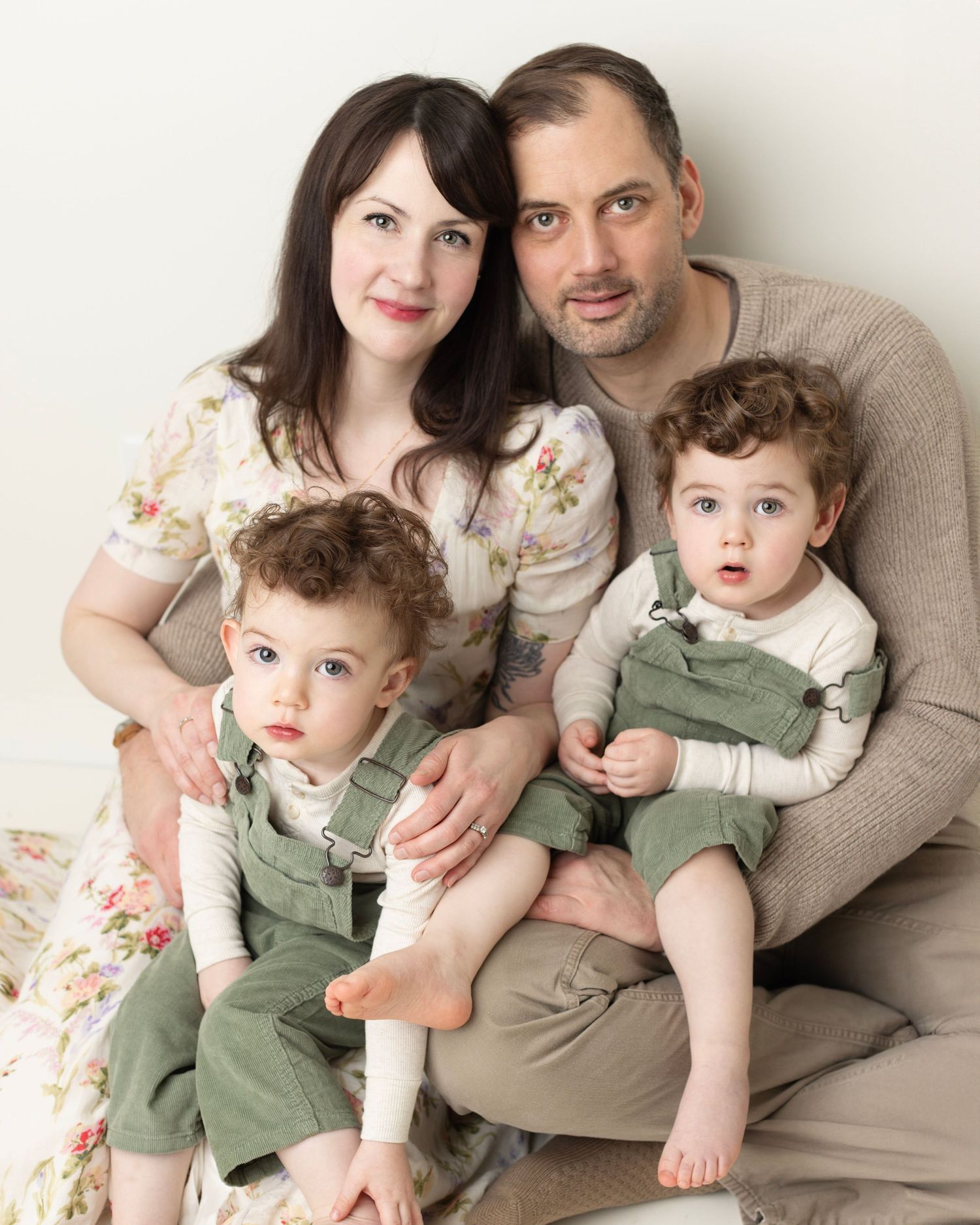 A family of three poses together on a beige couch in coordinated outfits for a professional portrait session.