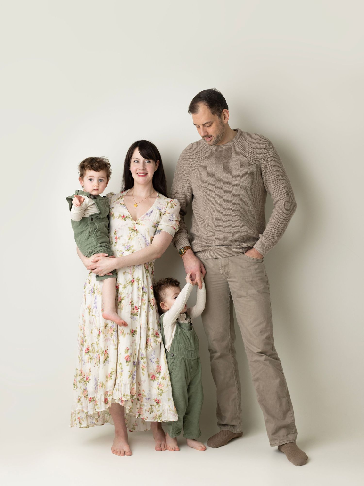 Family wearing coordinated neutral tones poses together against white background in casual studio portrait.